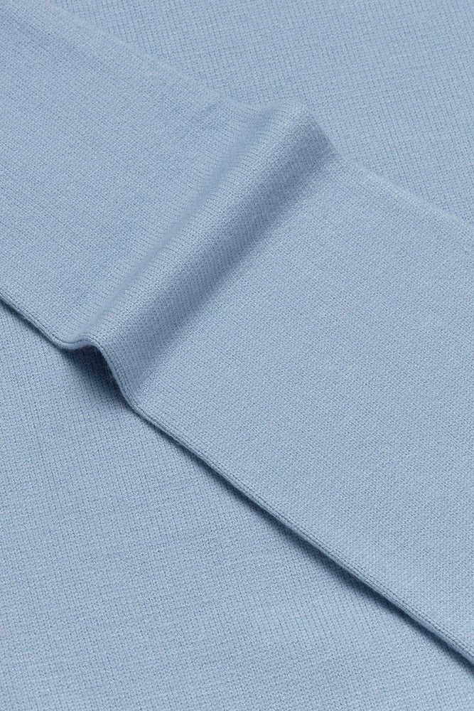 Stoffdetaljer av elegant lyseblå genser med kabelstrikket bol og glatte ermer. Halv-zip åpning i halsen. Foto